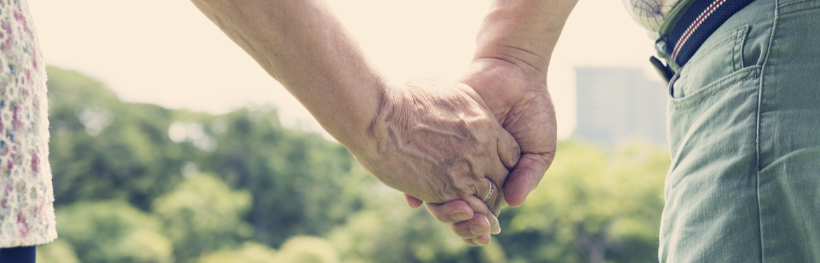 A close up of an older couple holding hands in a park