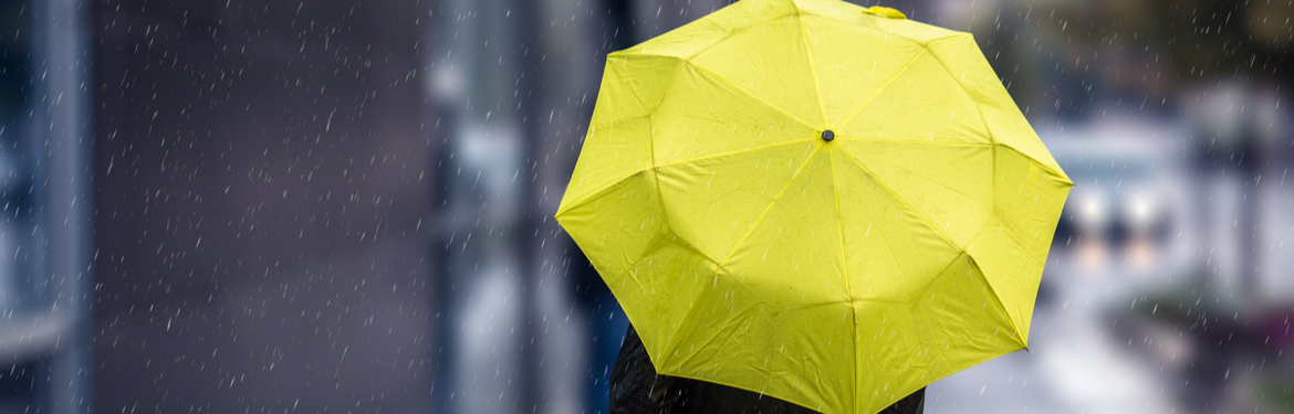 A person holding a yellow umbrella as they walk down a street