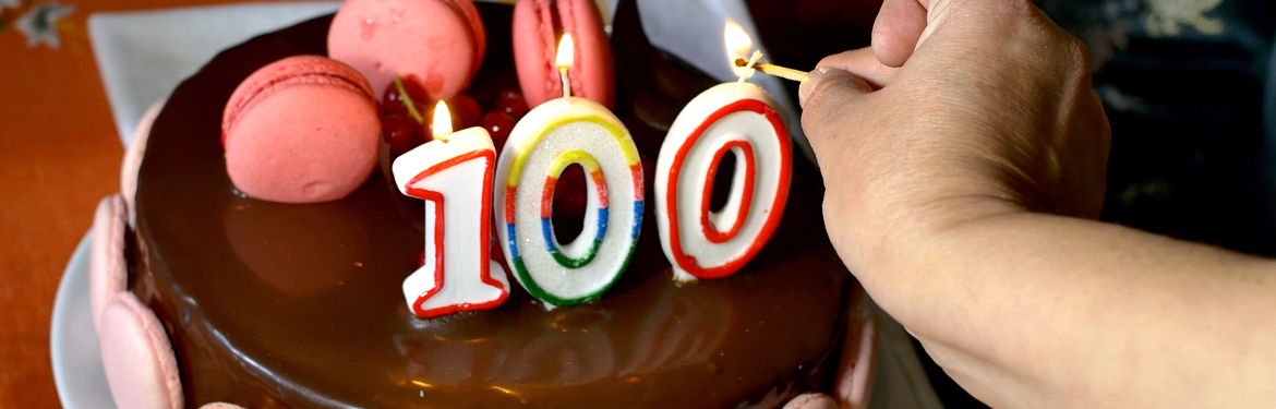 Someone lighting candles on a 100th birthday cake.