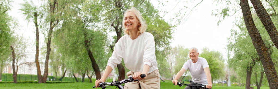 An elderly couple riding their bikes in the park.