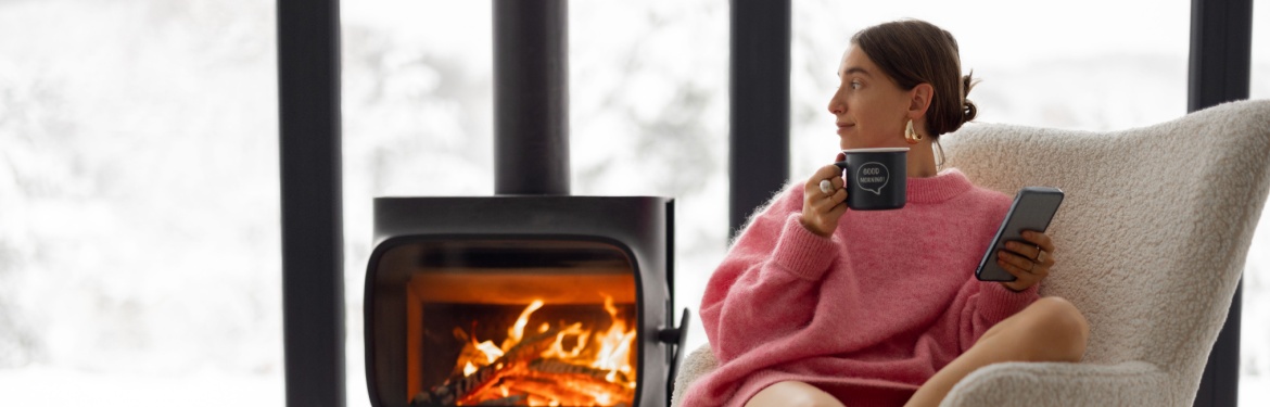 Woman sitting in a chair with a wood fire behind her.