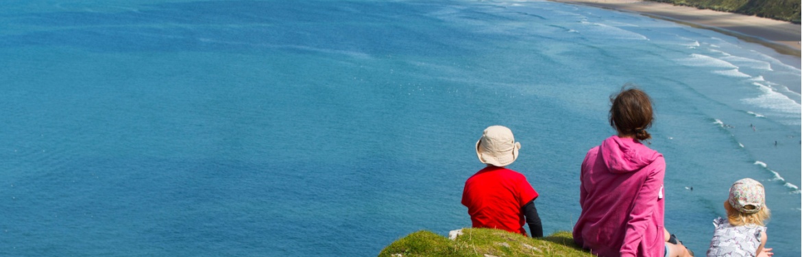 A family sitting on a clifftop overlooking a beach.