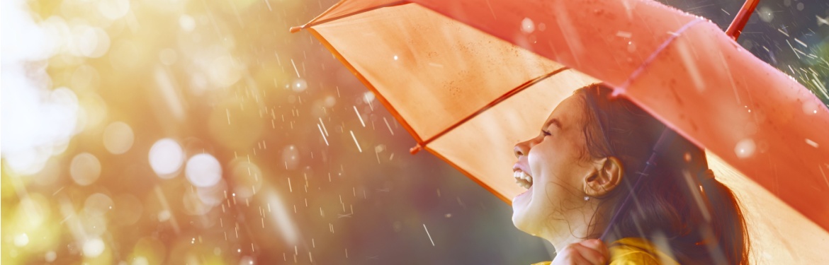 A girl laughing in the rain under an umbrella.