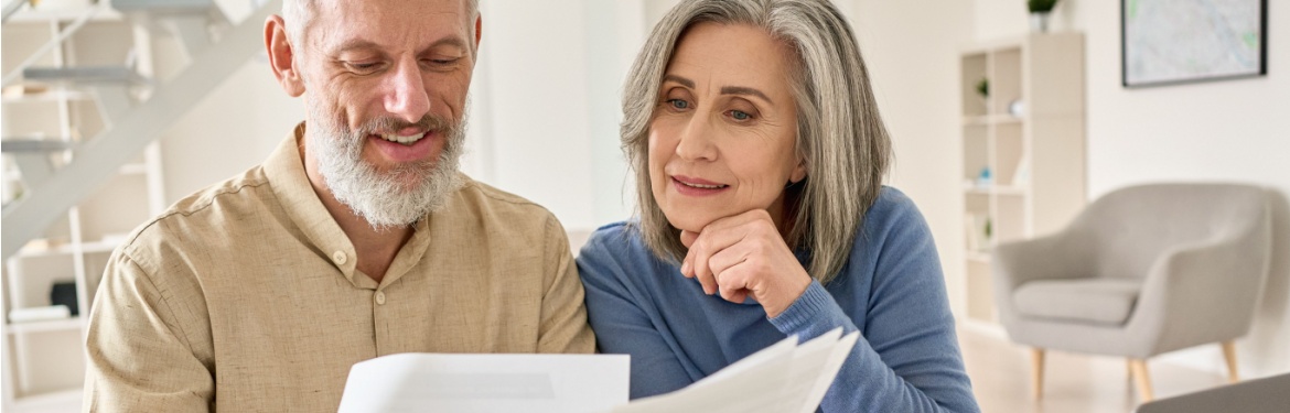 A senior couple sit at a laptop comparing multiple documents
