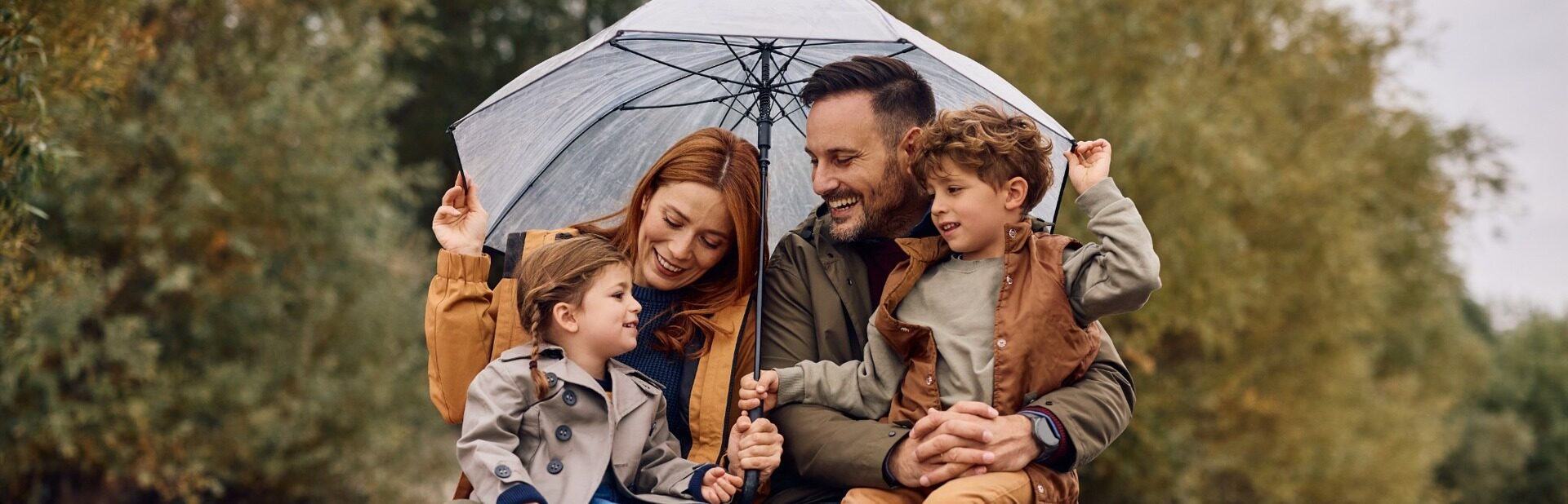 A young family sheltering under an umbrella and smiling