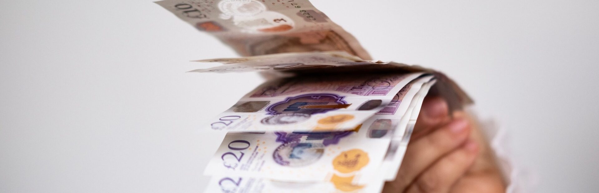 A hand holding UK bank notes.