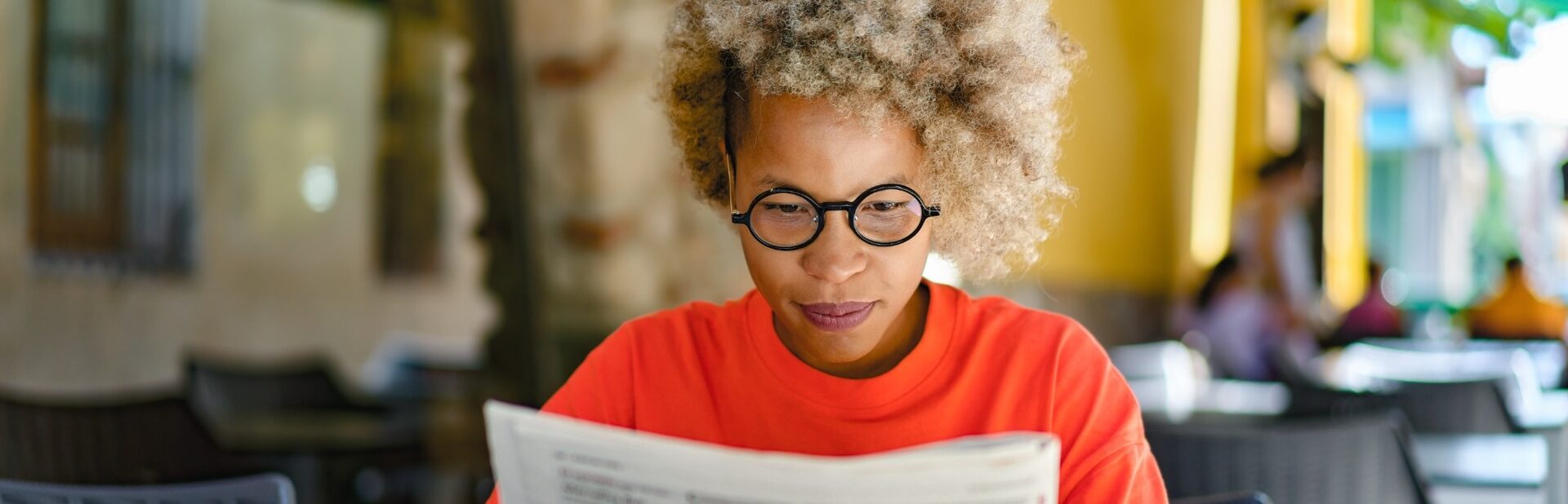 A woman reading a newspaper in a café.